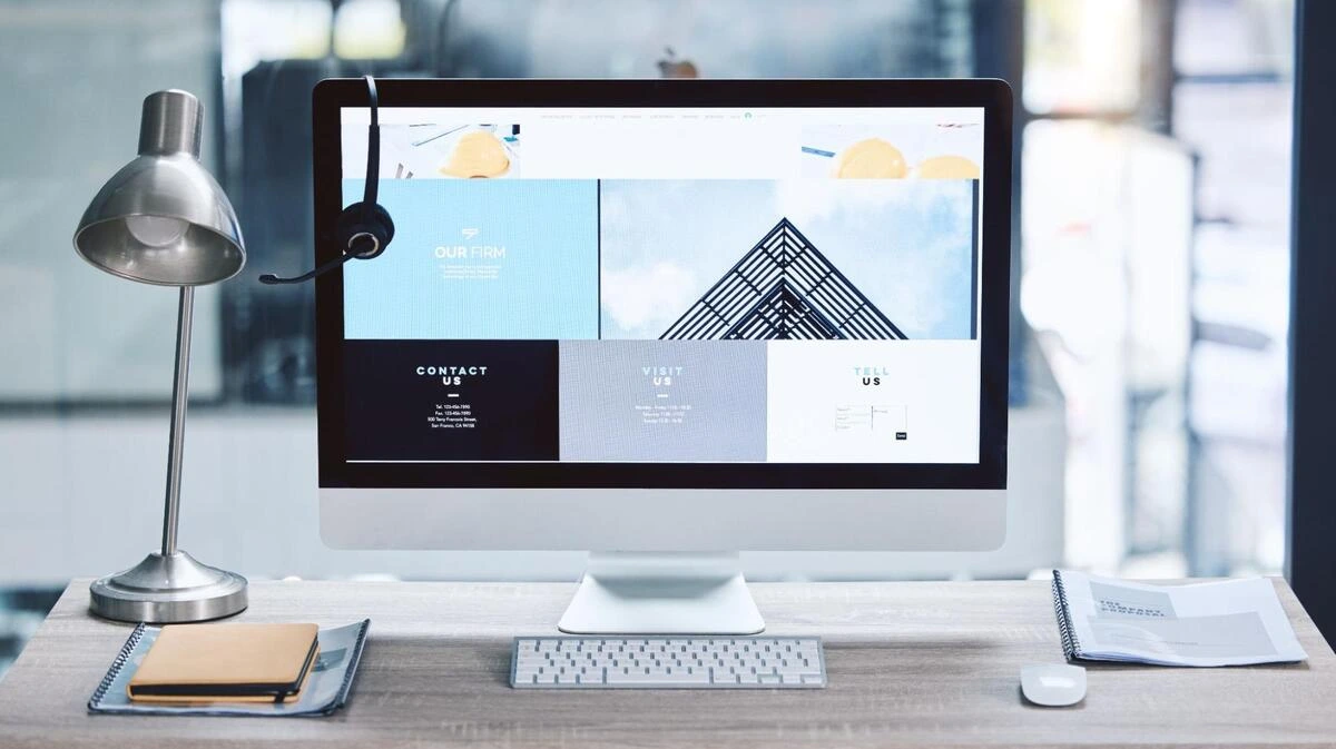 Small Business Website Planning and Design Computer monitor displaying a website design layout with a lamp and a notebook on a desk