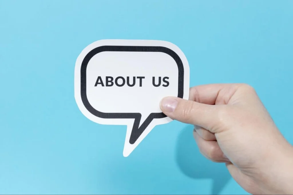 Hand holding a speech bubble sign that reads About Us against a blue background