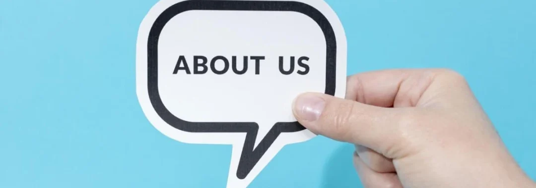 Hand holding a speech bubble sign that reads About Us against a blue background